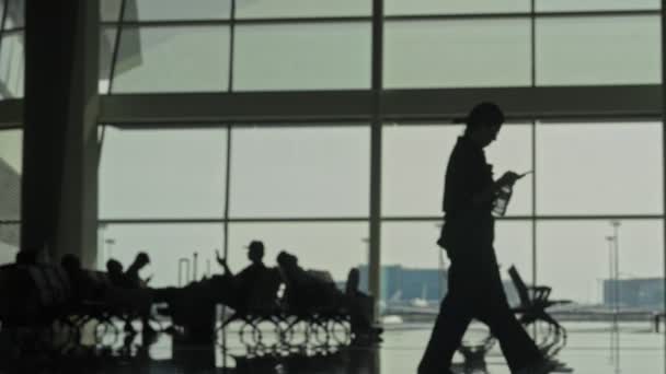 Nierozpoznawalne rozkojarzonych pasażerów sylwetki spaceru, siedzi w poczekalni na lotnisku — Wideo stockowe