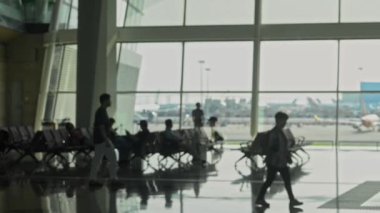 Şehirdeki uluslararası havaalanı binasında oturan ve yürüyen tanınmayan erkek ve kadın yolcular.