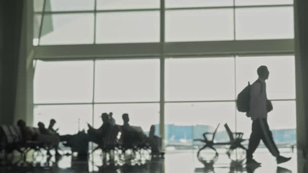 Unrecognizable silhouttes of people with baggage walking in airport waiting room. blurred defocused shot — Stock Video