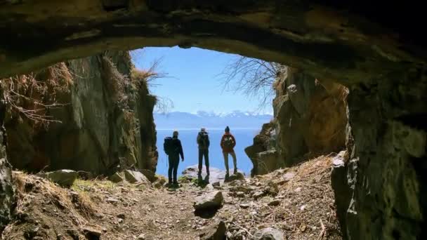 Трое туристов наслаждаются красивой природой, стоя на берегу моря в весенний день — стоковое видео