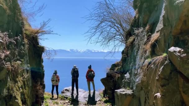 Punto di vista di viaggio tre escursionisti con zaino in piedi sulla roccia bordo guardando il lago baikal punto di riferimento — Video Stock