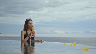Güzel kızıl saçlı kadın Bali tatil köyündeki okyanus havuzunda egzotik kokteyl içiyor..