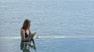 Genç Amerikalı kadın Bali Adası 'ndaki okyanus havuzunda dinlenirken akıllı telefon kullanıyor..