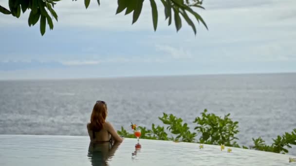 Vista posteriore di donna rilassante in piscina a sfioro con cocktail drink. concetto nuoto, orizzonte — Video Stock