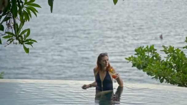 Молодая сексуальная женщина пьет коктейль в бесконечном бассейне. женщина на балийском курорте на океане — стоковое видео