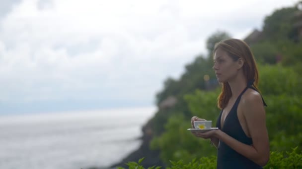 Young american red haired woman drinking tea standing on coast during traveling on tropical island. — 비디오