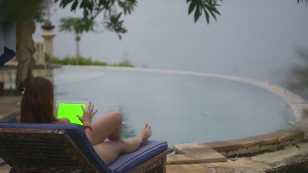 Nő fekvő pázsit szék medence mellett, és használja tabletta zöld modell képernyő üdülőhely bali hotel. — Stock videók