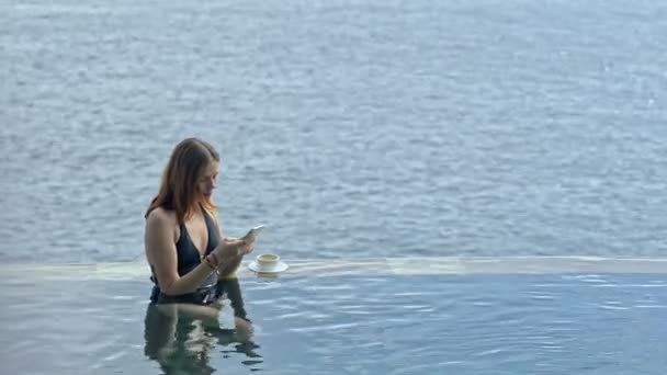 Mladá americká žena pomocí smartphone odpočinku v oceánu bazénu na ostrově Bali. — Stock video