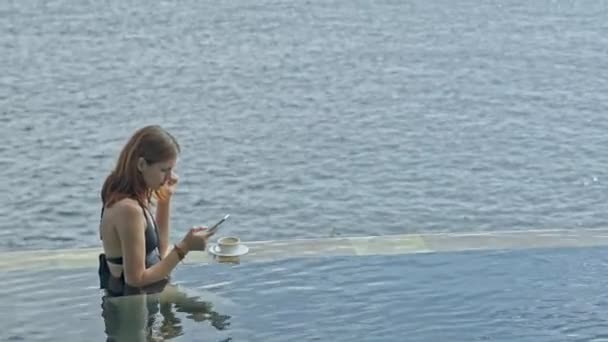 Woman in swimming pool using smartphone. female on bali resort on ocean background surfing internet — 비디오