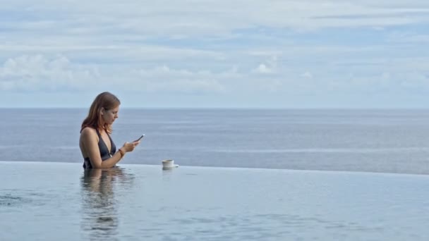 Kobieta w nieskończoność basen z kawą i trzymając telefon komórkowy, aby zrobić zdjęcie. dość sexy kobieta zrelaksować — Wideo stockowe