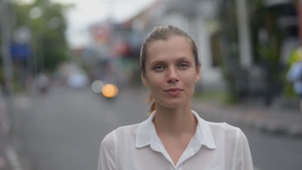 Nahaufnahme einer jungen hübschen kaukasischen Frau, die lächelnd in die Kamera blickt und auf der Straße in Bali posiert — Stockvideo