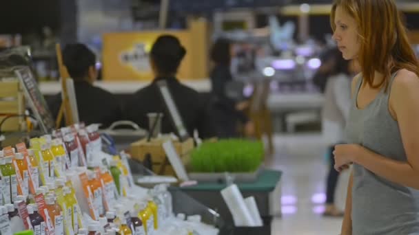 Jovem mulher em supermercado de alimentos saudáveis escolhendo suco de bebida orgânica em garrafa — Vídeo de Stock