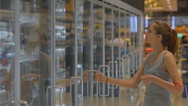 Mujer joven de compras en el supermercado abriendo nevera para tomar bebidas de alimentos refrigerados. zumo — Vídeo de stock