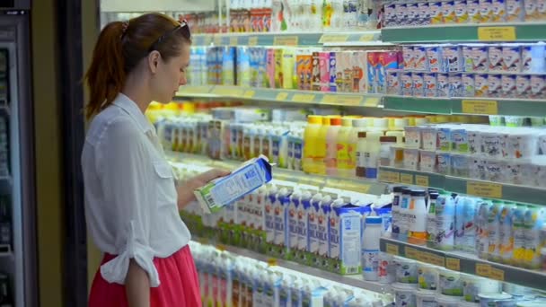 Bali, Indonesia - March, 2019: Young woman shopping in supermarket take milk in cardboard box from refrigerator. shopping — Stock Video