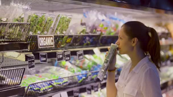 Young woman shopping in grocery store. Choosing fresh green salads and organic vegetables — 비디오
