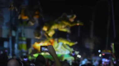 Hareket eden hayvan siluetiyle gece festivali. İnsanlar ellerinde cep telefonlarıyla video kaydediyor, fotoğraf çekiyorlar.