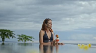 Genç seksi kadın sonsuz yüzme havuzunda kokteyl içer. Kadın Bali tatil köyü palmiye ağacı geçmişi