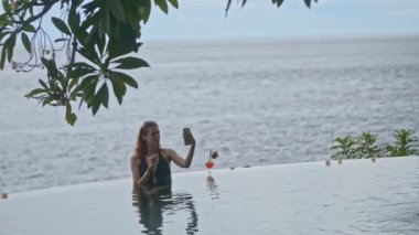 Kadın selfie çekiyor, telefonuyla sonsuz havuzda fotoğraf çekiyor. Kavram zekası, dalgalanma, sonsuzluk. Bali Oteli