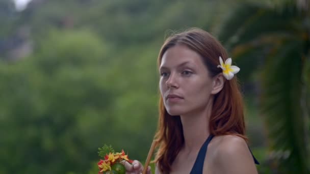 Frau genießt tropischen Cocktail. lächelt lächelnd in die Kamera. im Dschungel und unter Palmen — Stockvideo