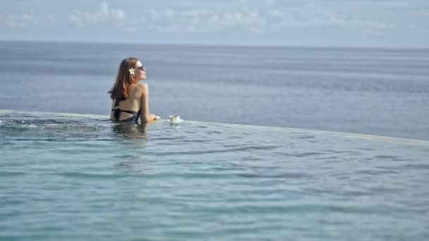 Joven mujer sexy tomando el sol en la piscina infinita. hembra en Bali resort en el fondo marino — Vídeos de Stock