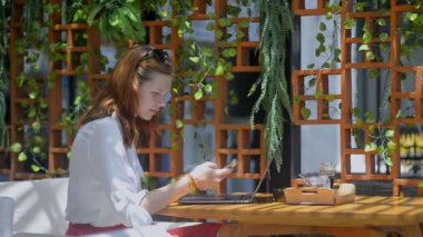 Elinde telefon olan genç bir kadın bir kafede dinleniyor. Restoran masasında dizüstü bilgisayar