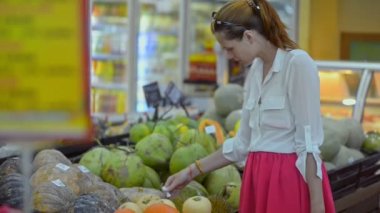 Genç kızıl saçlı alışverişçi Asya süpermarketinde dikilirken egzotik meyveleri seçiyor..
