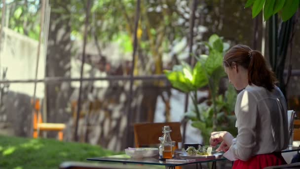 Жінка їсть тост авокадо у відкритому кафе. жінка на фоні курортної відпустки пальми — стокове відео
