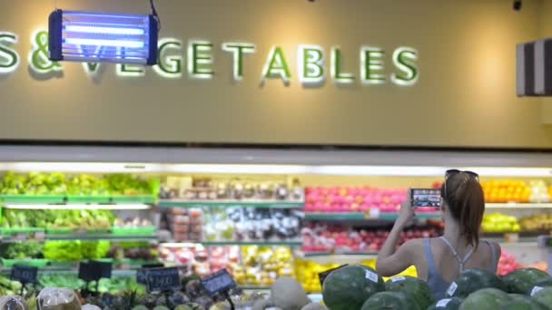 Mujer joven haciendo fotos de pie en la sección de verduras y frutas en la tienda. — Vídeo de stock