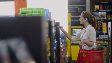 Bali, Endonezya - Mart 2019: Genç bir kadın süpermarketin içinde duran kadın ürünlerini seçiyor. Müşteri saklama paketi