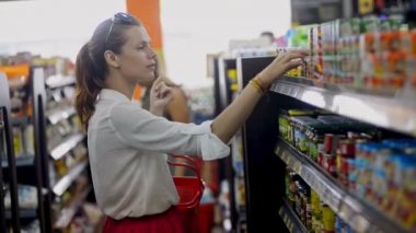 Bali, Endonezya - Mart 2019: Kavanozu ve konserve yiyeceği seçen ve septe, alışveriş arabasına koyan genç bir kadın. dükkan koridorunda