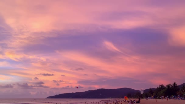 Dramatyczny różowy zachmurzony zachód słońca. Wieczór na zatłoczonej plaży z turystami. turyści pływają w morzu — Wideo stockowe