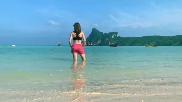 Вид ззаду підходить для туриста-жінки, що стоїть у морській воді на пляжі в Таїланді. сонячний день — стокове відео
