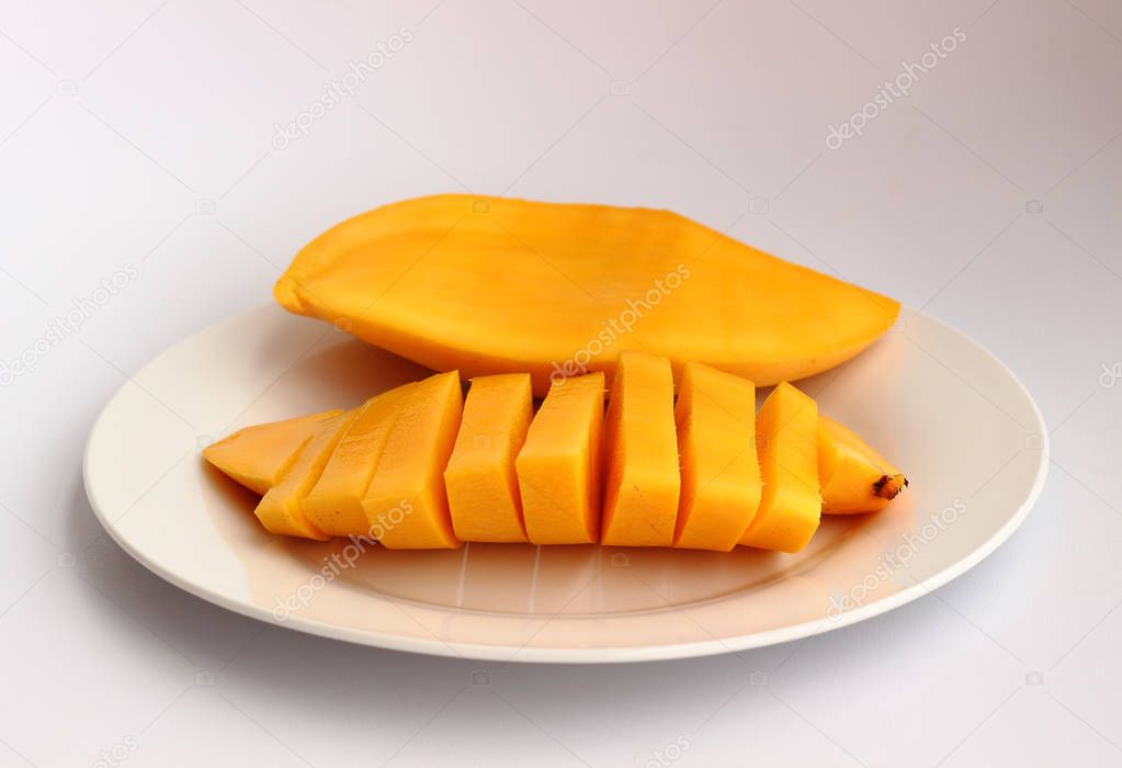 Isolated juicy yellow Thai mango on the white round dish on light background with soft shadows. Front view
