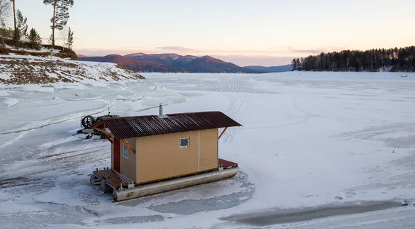 Winter landscape of mobile change house \'checkpoint\' on skis drag platform on the ice surface of a frozen lake in dusk