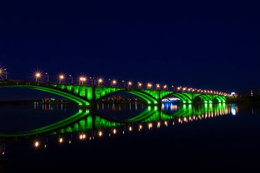 Rusya 'nın Krasnoyarsk kentindeki Yenisei Nehri üzerindeki ortak köprü. Köprünün yansıması ve sudaki aydınlanma. Krasnoyarsk şehrinin gece ışıkları. Gece şehir manzarası. Şehir Işıkları