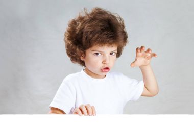 Küçük çok kıvırcık saçlı çocuk kameraya çağrıştırıyor. Gri arka plan. Yakın çekim.