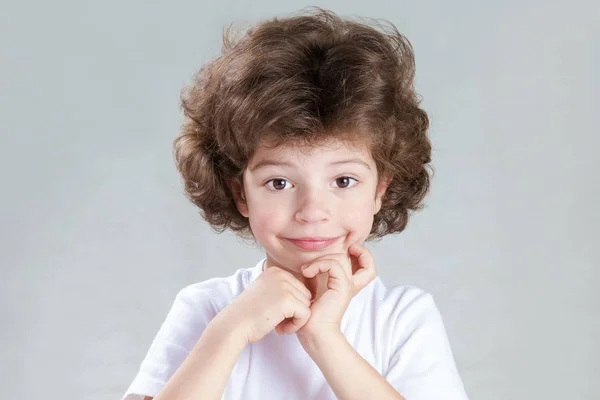 Encantador niño de pelo rizado con una camisa blanca mira a la cámara. Fondo gris. Primer plano . — Foto de Stock