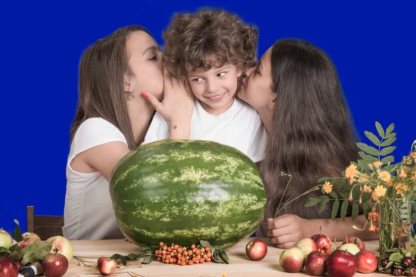 A nővérek suttogás a fül a kis testvére göndör. Előttük fekszik egy hatalmas egész görögdinnye gyümölcs. Közeli kép:. — Stock Fotó