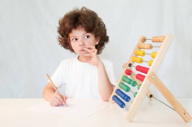 Görevin çözümün bir beyaz gömlek düşüncesinde sevimli kıvırcık saçlı çocuk. Gri arka planı.