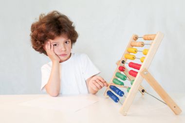 Sevimli çocuk puanları gösteren bir kalem ile ağlayan. Kameraya bakıyor. Masaya oturur. Gri arka planı.