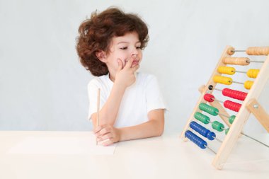 Sevimli kıvırcık saçlı çocuk elinde bir kalem ile onun parmağı analog hesap makinesi arıyorum bir sırıtma ile dudaklarına bastırdı. Yakın çekim. Gri arka planı.