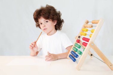 Elinde kalem ile sevimli kıvırcık saçlı çocuk düşünceli fotoğraf makinesine benziyor. Yakın çekim. Gri arka planı.
