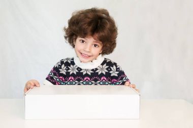 Bir kazak kameraya bakarak bir ilgi ile bir süsleme ile mutlu sevimli çocuk. Beyaz kutu elele. Gri arka planı.