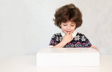 Düşünceli genç yakışıklı bir kazak ile süs parmağını, ısırma beyaz kutu bakar. Gri arka planı.