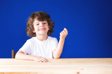 Kameraya bakarak mutlu kıvırcık yakışıklı yumruk sıkılı. Yakın çekim. Mavi arka plan.