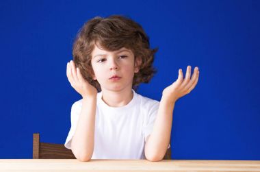 Kıvırcık sevimli çocuk onun eller, avuç içi kadar dikkatle kameraya bakarak kaldırdı. Mavi arka plan.