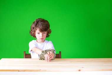 Ellerini masadan kıvırcık yakışıklı zinciri tarafından bağlı ve ne yazık ki kameraya benziyor. Yakın çekim. Yeşil arka plan.