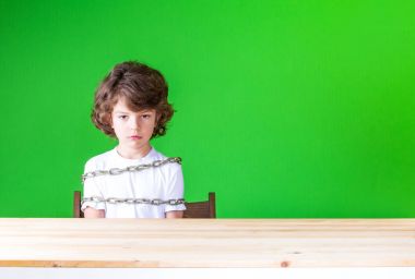 Masada oturan kıvırcık yakışıklı bir zincir sarılı ve ne yazık ki kameraya benziyor. Yakın çekim. Yeşil arka plan.