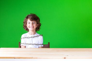 Masada oturan kıvırcık sevimli çocuk gülüyor ve kamera seyir bir zincir sarılı. Yakın çekim. Yeşil arka plan.