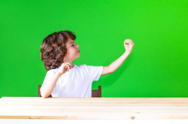 Elini yarı açık bir masada oturan kıvırcık sevimli çocuk kaldırdı, sıkışık palm saman. Yakın çekim. Yeşil arka plan.